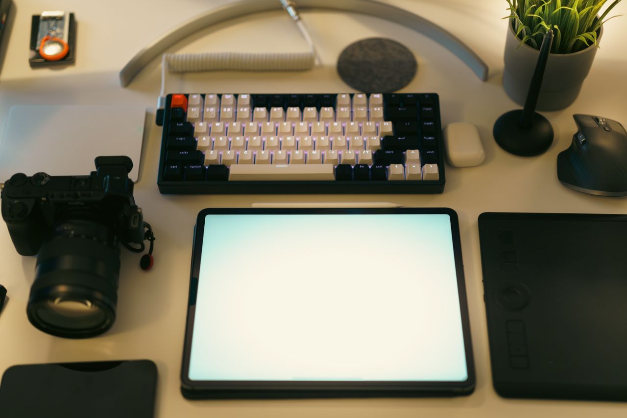 A chic desk arrangement with a digital tablet, keyboard, camera, and plant, perfect for creative work.